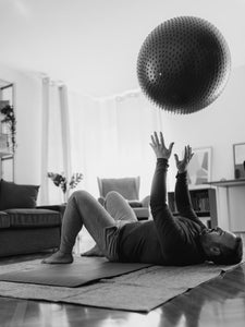 Man lying on the ground tossing an inflatable exercise ball in the air above him.