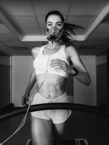 Woman wearing an endurance testing mask while running indoors on treadmill.